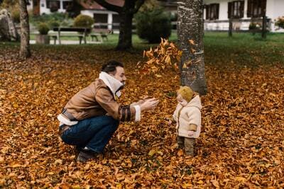 father and toddler girl playing in fall leaves