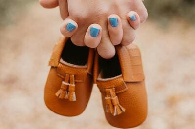 couple holding a pair of baby moccasins with woman's nails painted blue