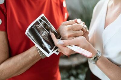two women holding hands and sonogram pictures and a pregnancy test