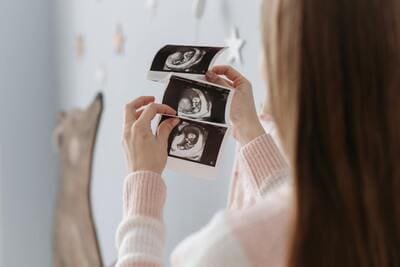woman in pink sweater holding ultrasound pictures